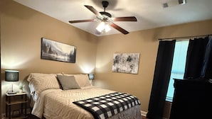 Un dormitorio con cama, ventilador de techo, decoración en la pared y ventana con cortinas.