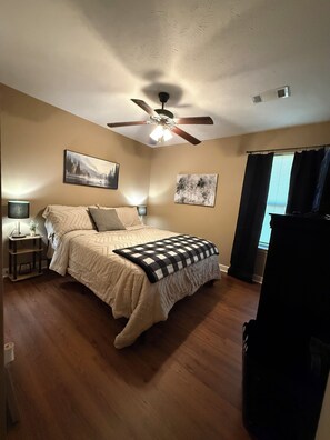 A bedroom with a bed, ceiling fan, wall art, and a window with curtains. - Wonderful 3-bedroom house with AC in peaceful Morrilton (Morrilton)