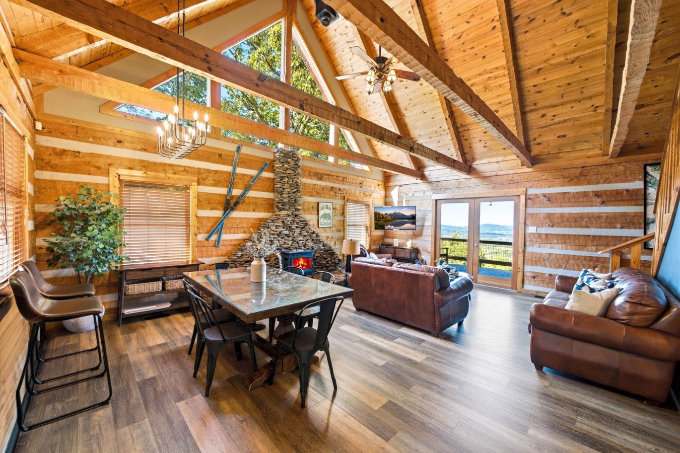 Interior de una cabaña de madera con chimenea de piedra, un comedor y un sofá.