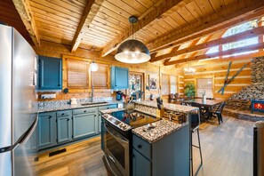 A spacious kitchen with granite countertops, a central island, and a stone fireplace. - Endless Views - Game Room, Arcade, Hot Tub! (Sevierville)