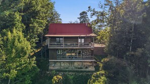 A two-story cabin with a red roof, surrounded by dense forest.