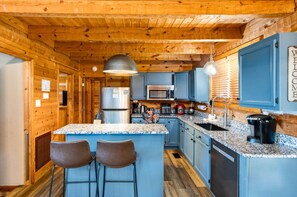 A cabin-style kitchen with a central island, bar stools, wooden walls, and a welcome sign.