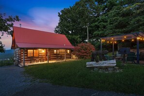 A log cabin with a red roof, a porch with seating, and a bear sculpture in the foreground.