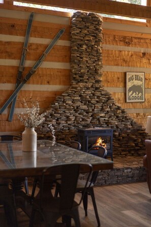 A rustic interior with a stone fireplace, wooden walls, and a dining area with chairs and a table.
