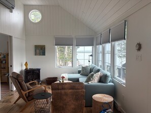 Een woonkamer met een bank, fauteuils, een bijzettafeltje en een raam met zonwering.