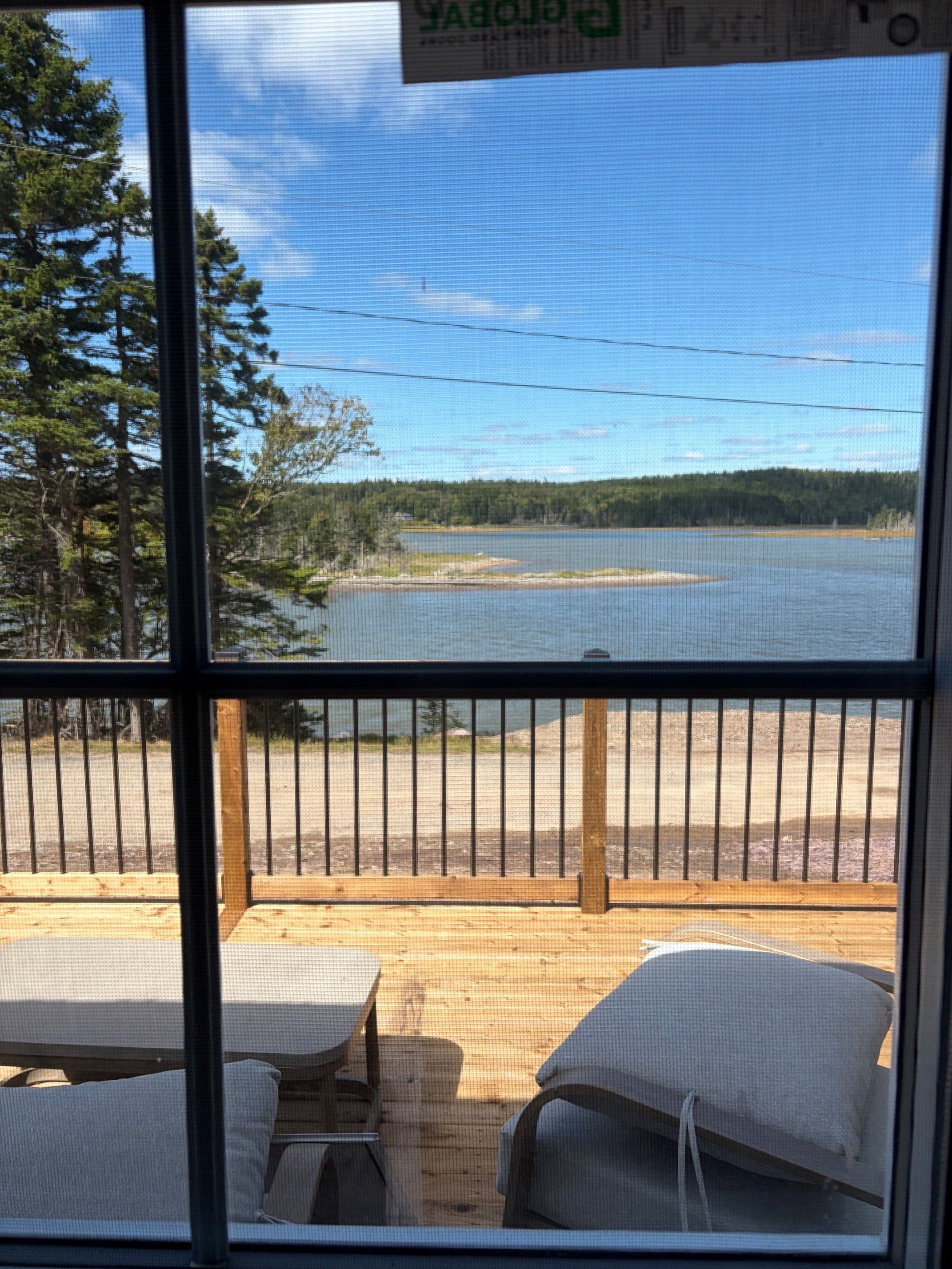 En utsikt från ett fönster med utsikt över en sjö, med en träveranda och stolar i förgrunden.