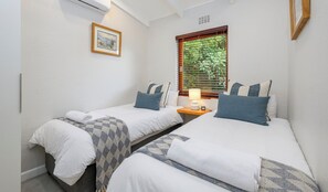 Una camera da letto con due letti, un comodino con una lampada, un quadro appeso al muro e una finestra con persiane.