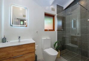 Un bagno moderno con un mobile lavabo bianco, un water, una doccia con pareti in vetro e uno specchio con illuminazione a LED.