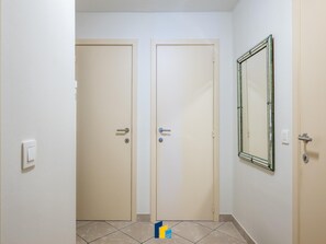 Ein Flur mit zwei geschlossenen Türen, einem Lichtschalter und einem Spiegel an der Wand.