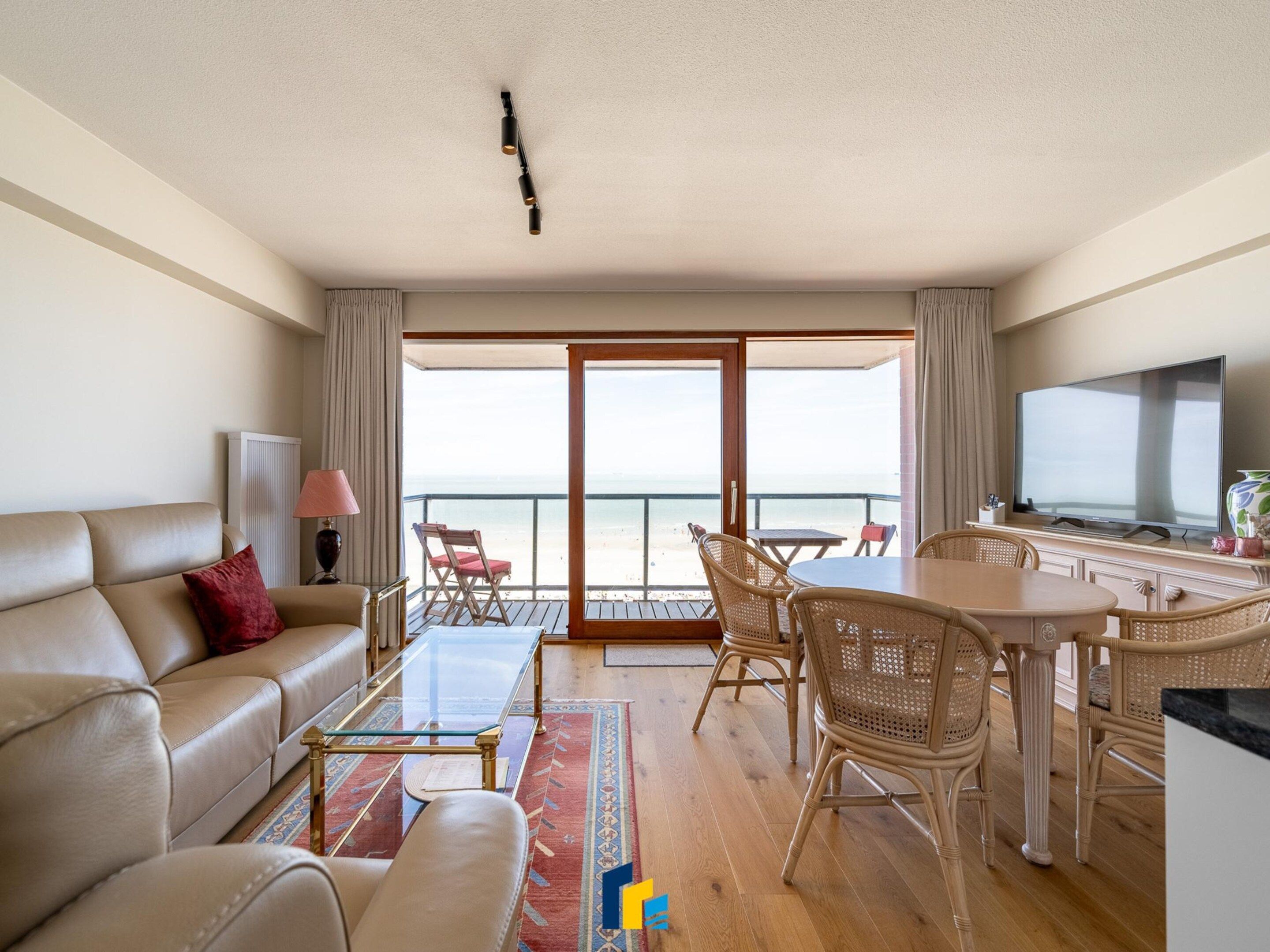 A hotel room with a balcony, a sofa, a dining table, and a TV.