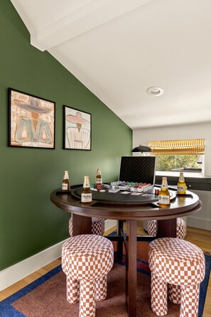 A room with a green wall, a round table with a laptop, Modelos beer bottles, and checkered ottomans. - Eastside ATX Social | Golf Sim • Hot Tub • Sauna (Austin)