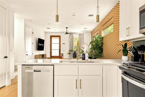A modern kitchen with a large island, stainless steel appliances, and a checkered wall pattern. - Eastside ATX Social | Golf Sim • Hot Tub • Sauna (Austin)