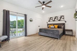 Ein Schlafzimmer mit einem Bett, einem Deckenventilator, einem Fenster mit Vorhängen und Blick ins Freie.