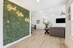 Ein modernes Wohnzimmer mit grüner Wand, Deckenventilator und Wand-Fernseher.