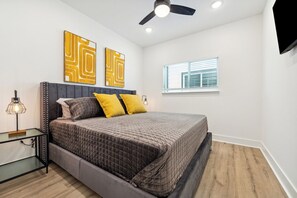 Un dormitorio con cama, mesita de noche, ventilador de techo y obra de arte en la pared.