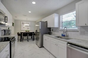 A modern kitchen with white cabinetry, a built-in oven, and a dining area with a table and chairs. - Home away from Home! (Spring)