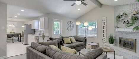 A living room with a gray sofa, a fireplace, and a kitchen in the background.