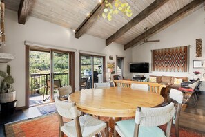 A spacious living area with a large wooden table surrounded by woven chairs, a television, and a decorative wall hanging. - Snowmass Retreat: Vaulted Ceilings, Wood FP, Balcony W/ Grill & Great Views, W/D, Parking, Pool & HT (Snowmass Village)