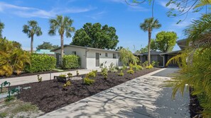 A residential area with a single-story house, a paved driveway, and a well-maintained garden with various plants and trees. - Seaturtle Cottage by Avantstay Lakefront + Firepit + Grill Vanderbilt Beach (Naples)