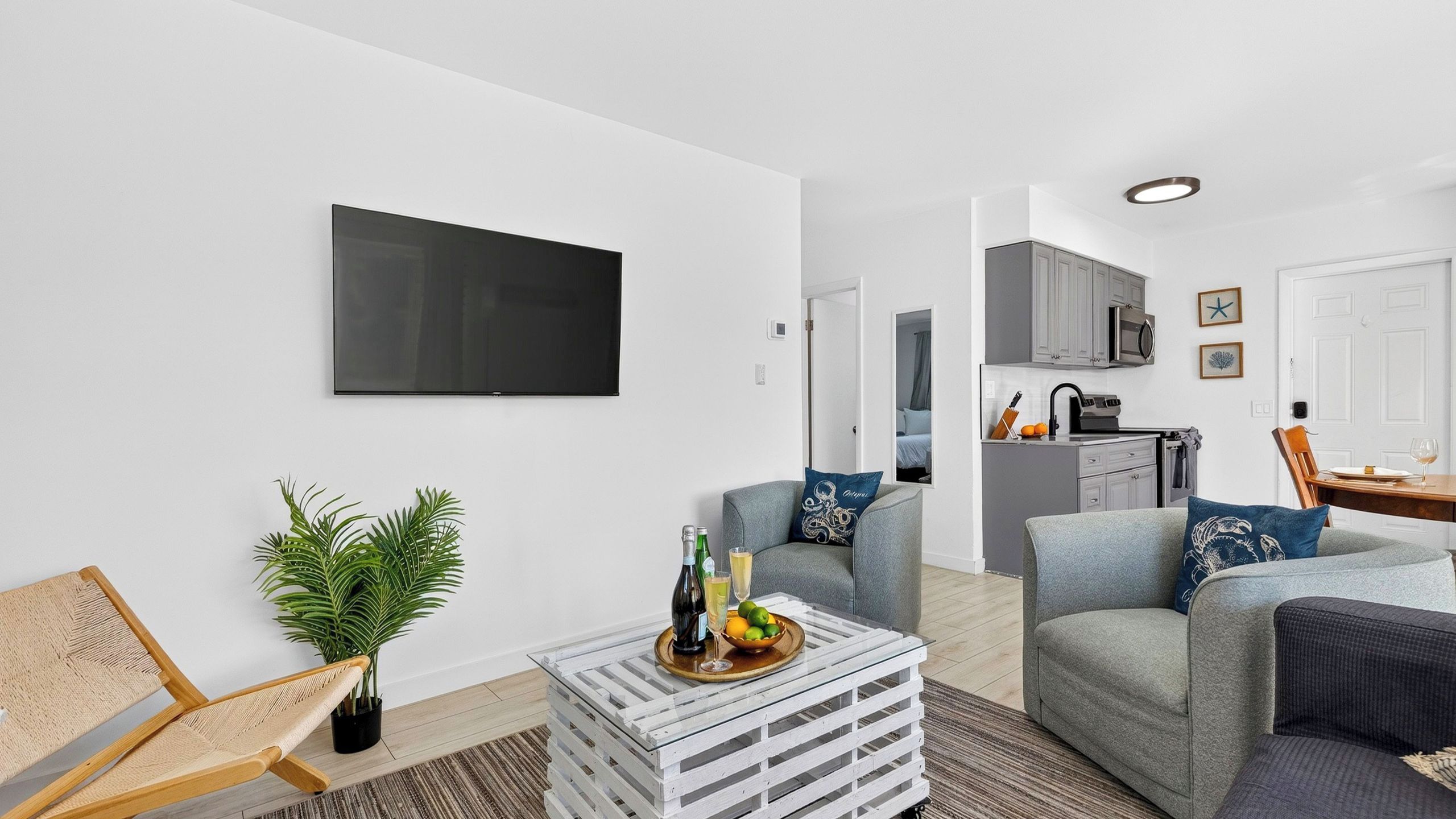 Uma sala de estar moderna com televisão de tela plana, uma mesa de centro com bebidas e um espaço de estar com sofá e poltronas.