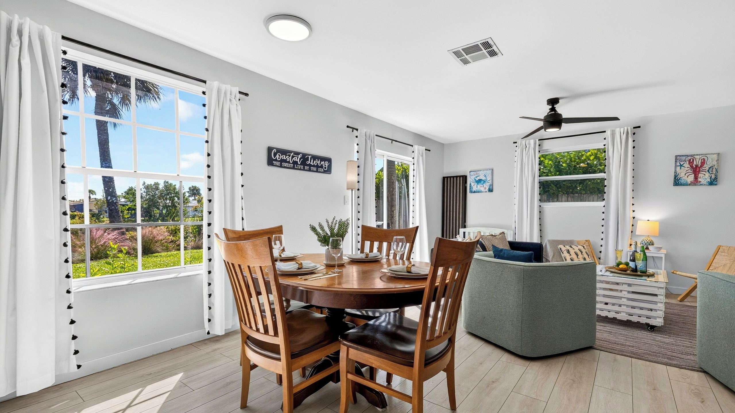 A dining area with a round table, four chairs, and a view of the outdoors through large windows.