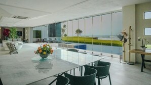 A modern interior with a large glass table and chairs, a decorative plant, and a view of the ocean. - Aurea Vita (Tres Vidas Acapulco Diamante)