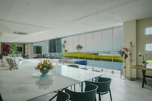 A modern interior with a large glass table and chairs, a decorative plant, and a view of the ocean. - Aurea Vita (Tres Vidas Acapulco Diamante)
