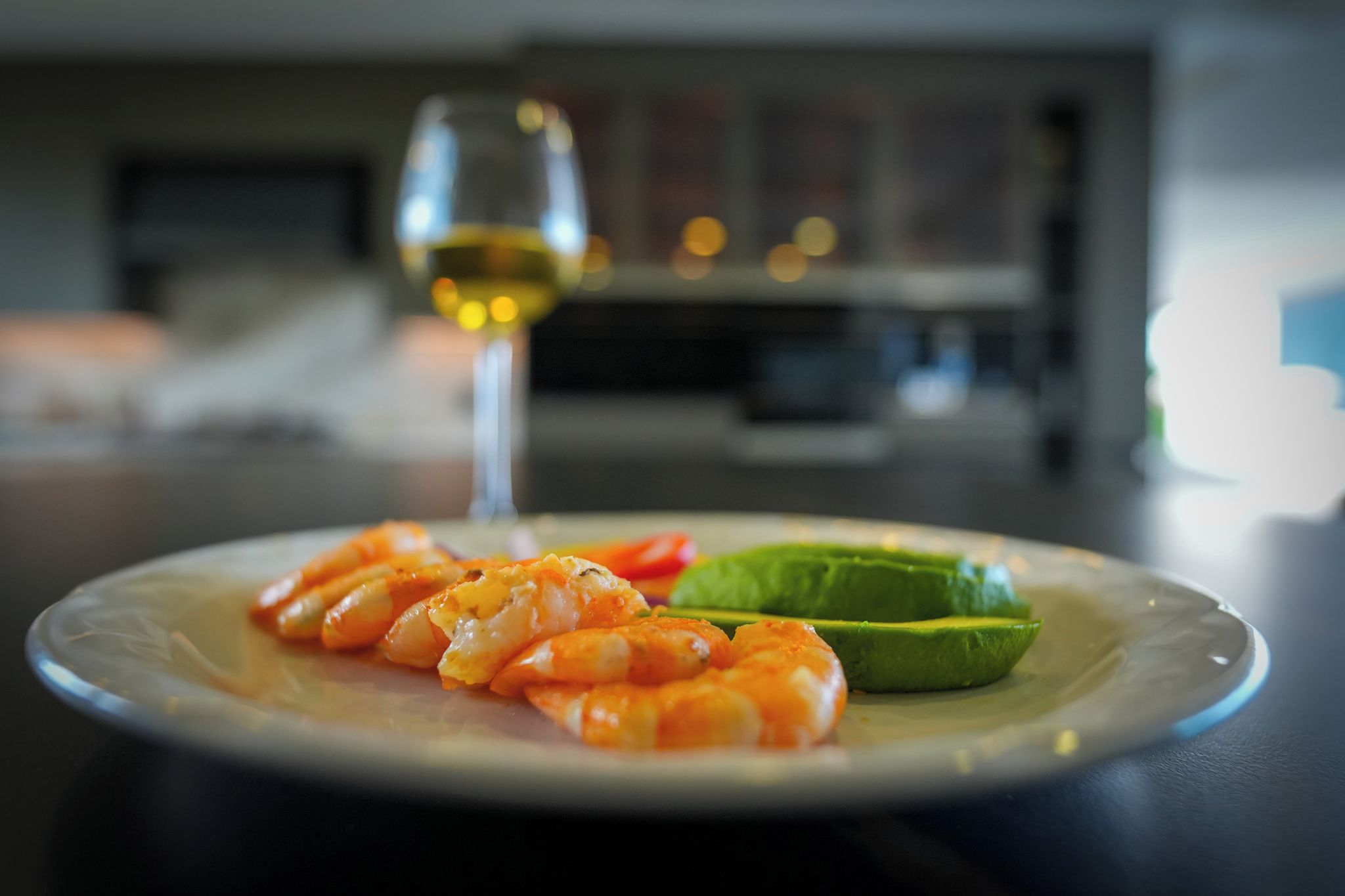 Un plato de camarones y aguacate sobre una mesa con una copa de vino blanco.