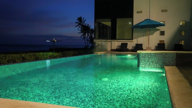 A swimming pool with clear water, a lounge area with chairs, and a view of the ocean at dusk. - Aurea Vita (Tres Vidas Acapulco Diamante)