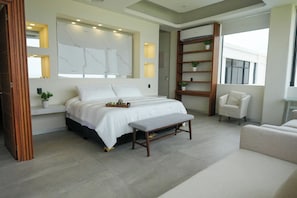 A modern bedroom with a bed, bedside tables, a bench, a chair, and a shelving unit with plants. - Aurea Vita (Tres Vidas Acapulco Diamante)