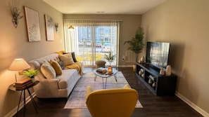 Una sala de estar con sofá, mesa de centro, mueble para televisión y vistas a través de un ventanal corredero.