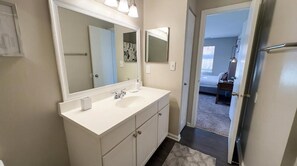 Un baño con tocador blanco, un espejo grande y una puerta que da a un dormitorio.