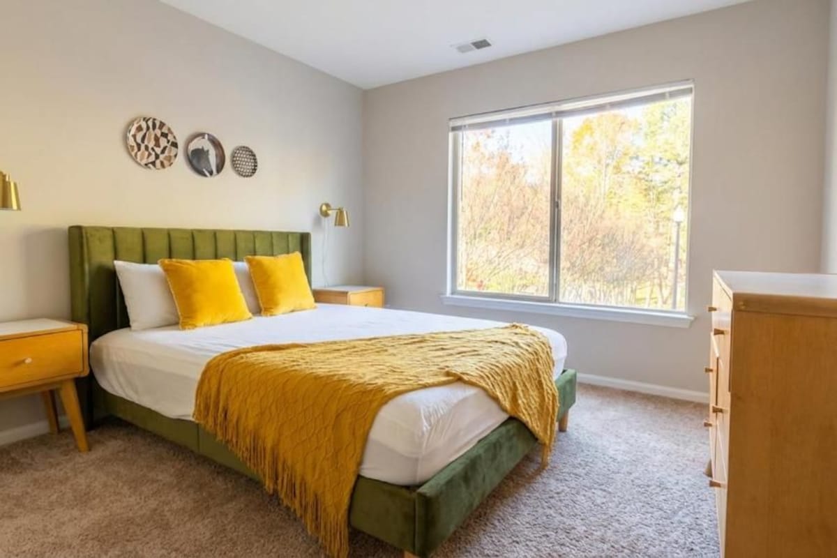 Un dormitorio con cama, mesitas de noche, cómoda y ventana con luz natural.