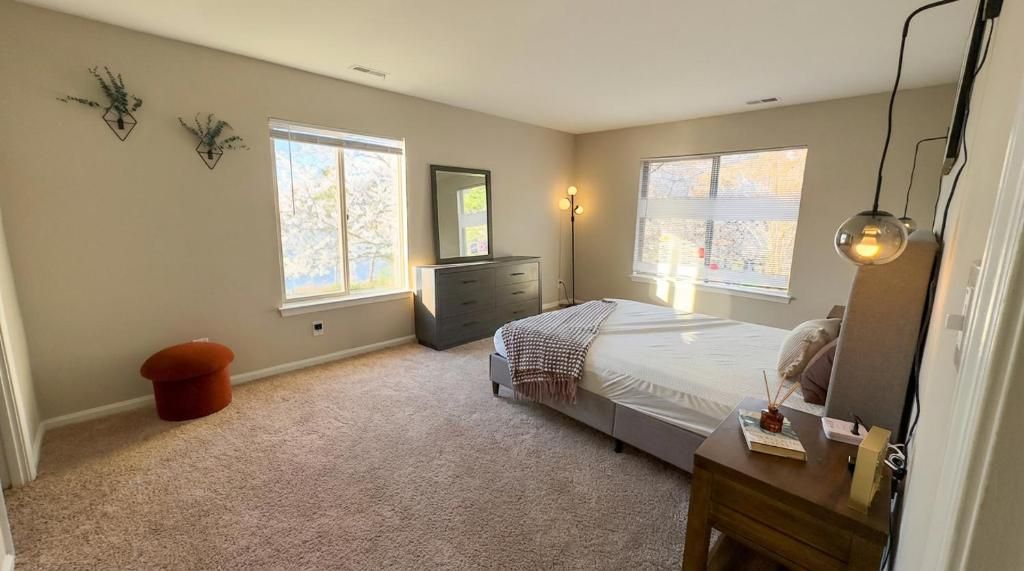 Un dormitorio con cama, cómoda y dos ventanas.