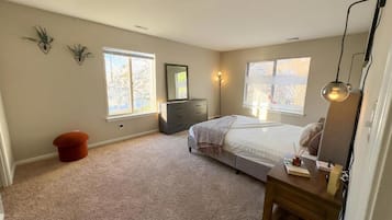 Un dormitorio con cama, cómoda y dos ventanas.