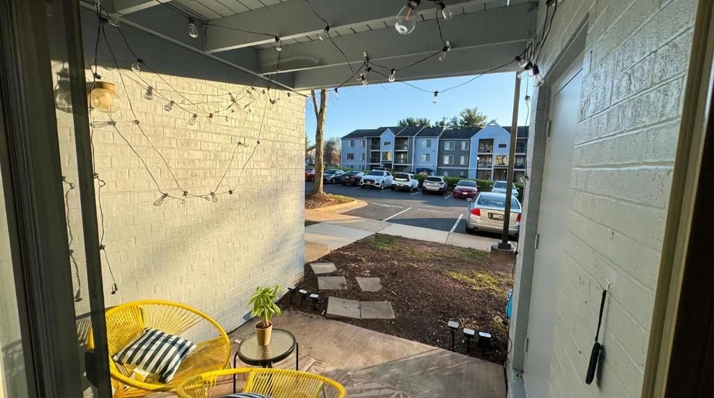 Un patio techado al aire libre con una silla amarilla, una mesita y una planta en maceta.