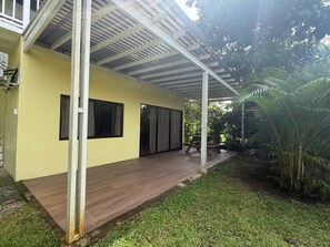 A covered outdoor area with a wooden deck, a yellow building, and a palm tree. - Casa Melda | Walk to the Beach & GandocaManzanillo (Manzanillo)