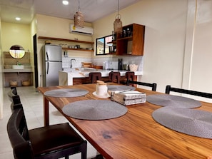 A modern kitchen with a wooden dining table, chairs, and a central island. - Casa Melda | Walk to the Beach & GandocaManzanillo (Manzanillo)