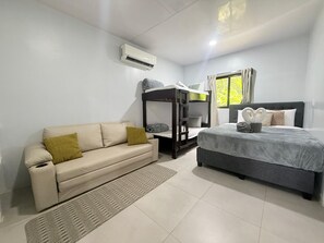 A hotel room with a bunk bed, a sofa, a bedside table, and a window with curtains. - Casa Melda | Walk to the Beach & GandocaManzanillo (Manzanillo)