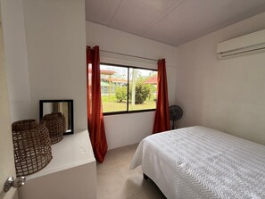 A bedroom with a bed, a window with curtains, a fan, and a mirror. - Casa Melda | Walk to the Beach & GandocaManzanillo (Manzanillo)