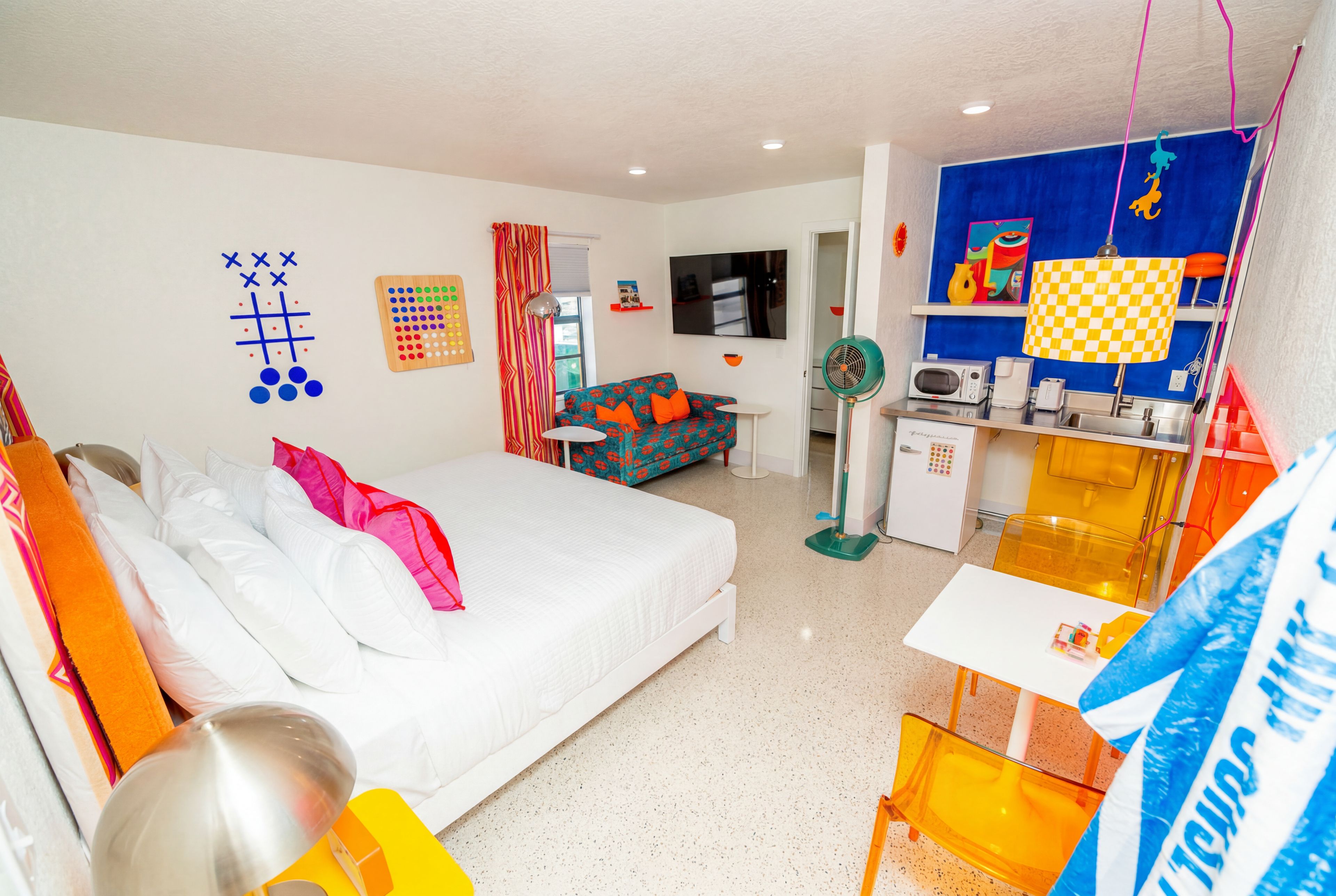 A hotel room with a bed, a sofa, a TV, a small table, and a kitchenette.