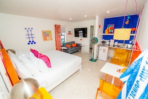 A hotel room with a bed, a sofa, a TV, a small table, and a kitchenette. - King Room in Treasure Island, just steps from Sunset Beach. (Treasure Island)