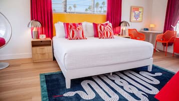 A modern bedroom with a large bed, a bedside table with a lamp, a small table with a lamp, and a chair.