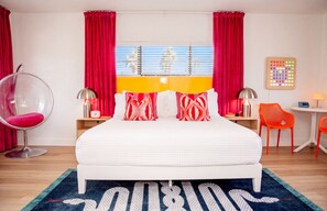 Une chambre moderne avec un grand lit, des rideaux rouges, un fauteuil suspendu, une petite table avec une lampe et un panneau lumineux fixé au mur.