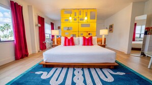 Une chambre d’hôtel avec un grand lit, des rideaux rouges, un tapis bleu et un élément de décoration jaune sur le mur.