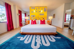 Une chambre d’hôtel avec un grand lit, des rideaux rouges, un tapis bleu et un élément de décoration jaune sur le mur.