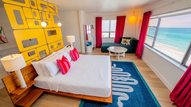 Une chambre d’hôtel moderne avec un grand lit, un petit canapé, une table basse ronde et une vue sur l’océan.