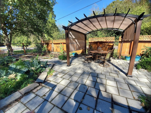 A garden patio with a pergola, a table with chairs, and potted plants.