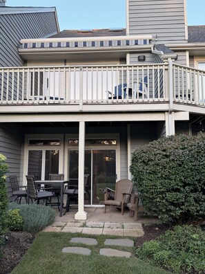 Ein zweistöckiges Haus mit überdachter Terrasse, Sitzgelegenheiten im Freien und einem gepflegten Garten.