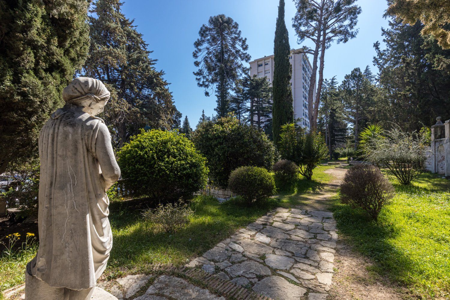 A statue in a garden with a stone pathway leading to a building.